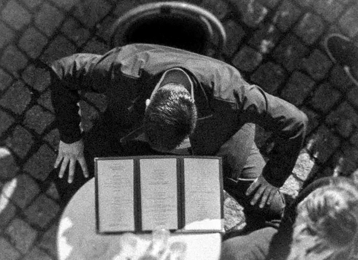 Overhead view of a man bending over a menu stand on cobblestones